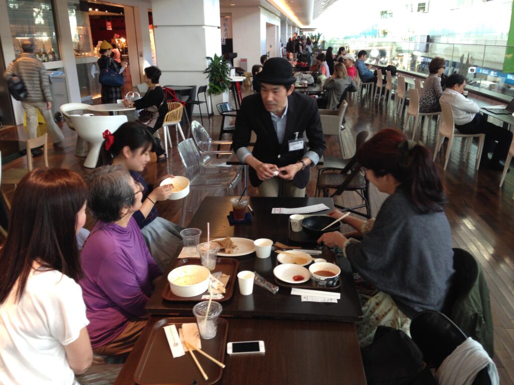 食事中の家族に出張マジシャンがカードマジックを披露 羽田空港 アッパーデッキトウキョウ６周年 記念イベント/ 出張マジシャンひろしつ